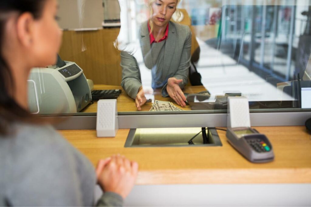 Teller counting cash for a customer behind a window for transaction security