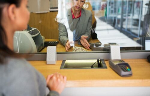 Teller counting cash for a customer behind a transaction security window