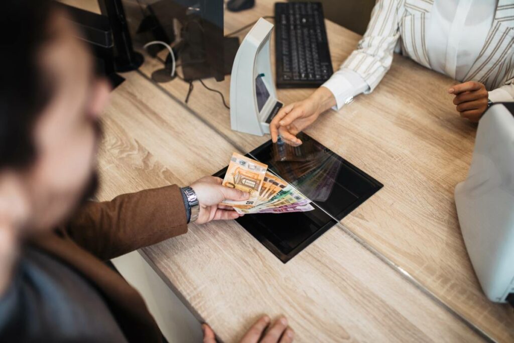 Man handing cash to a teller through a cash tray for transaction security