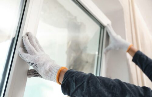Person wearing gloves pushing a large window pane into place